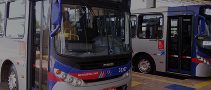 Foto de dois ônibus estacionados em um terminal metropolitano.